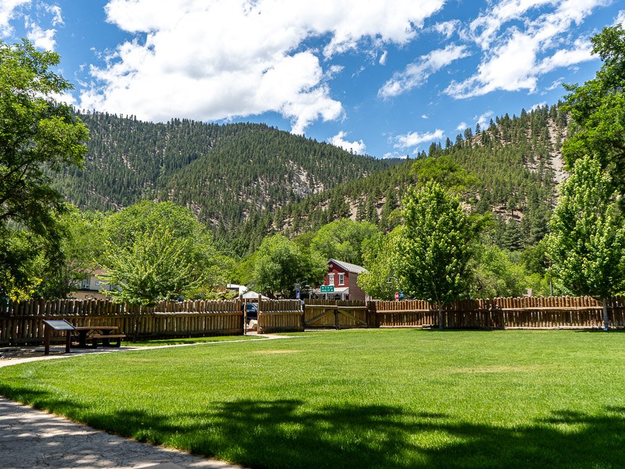 A photo showing the inside of the Mormon Station State Park, with lush green lawn in foreground with mountains and blue sky in the background.