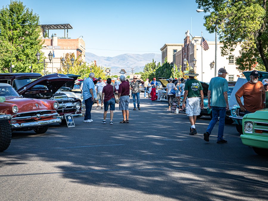 a community car show with cars lined up down the street, and people walking around